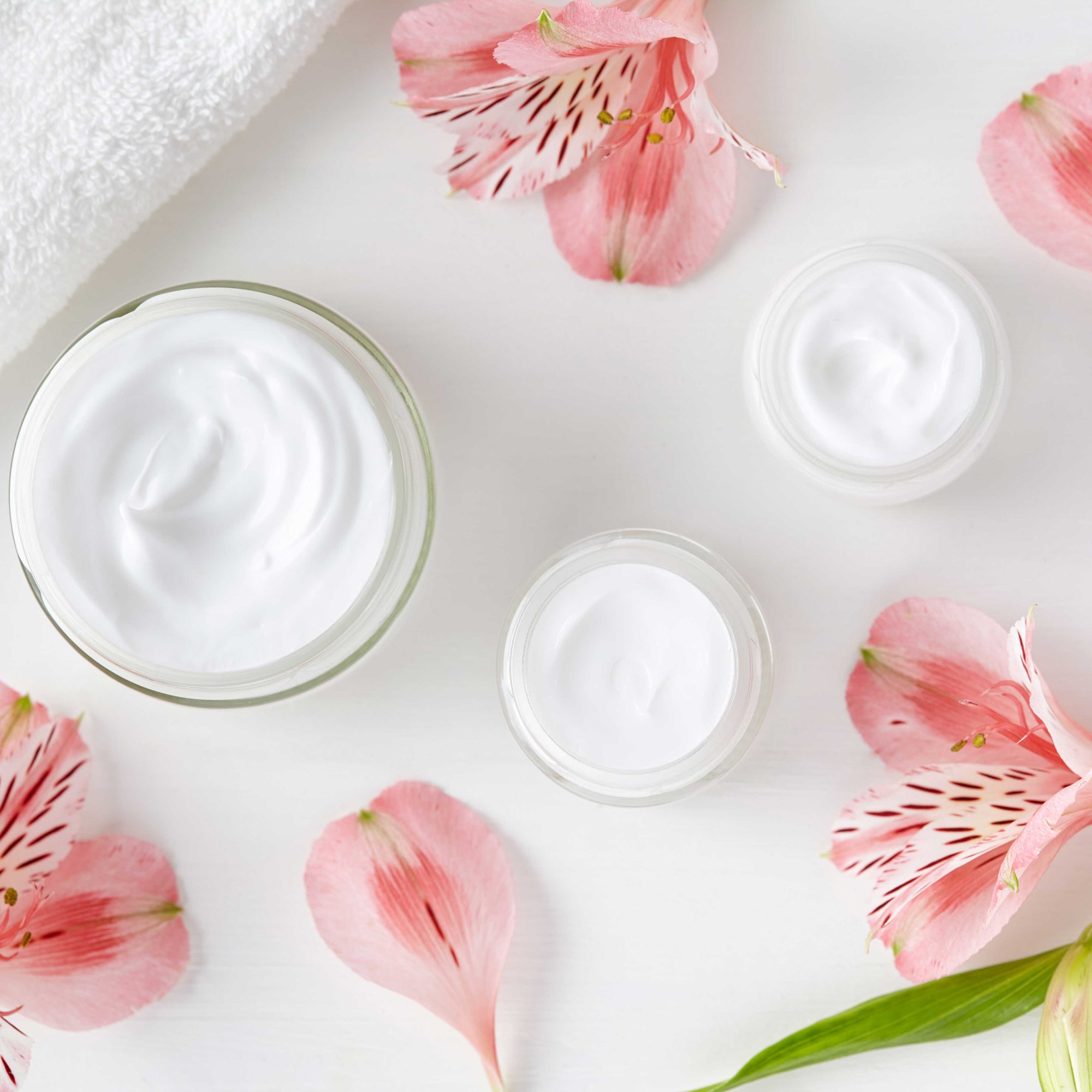 white cream and beauty products in round glass containers with pink flowers