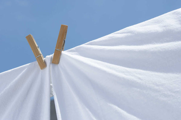 Two wooden clothespins holding a white sheet against a clear blue sky.