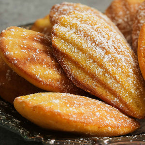 freshly baked madeleine cakes with powdered sugar; https://cdn.shopify.com/videos/c/o/v/f84e6300fb5e482ea9468c90ef686fca.mp4