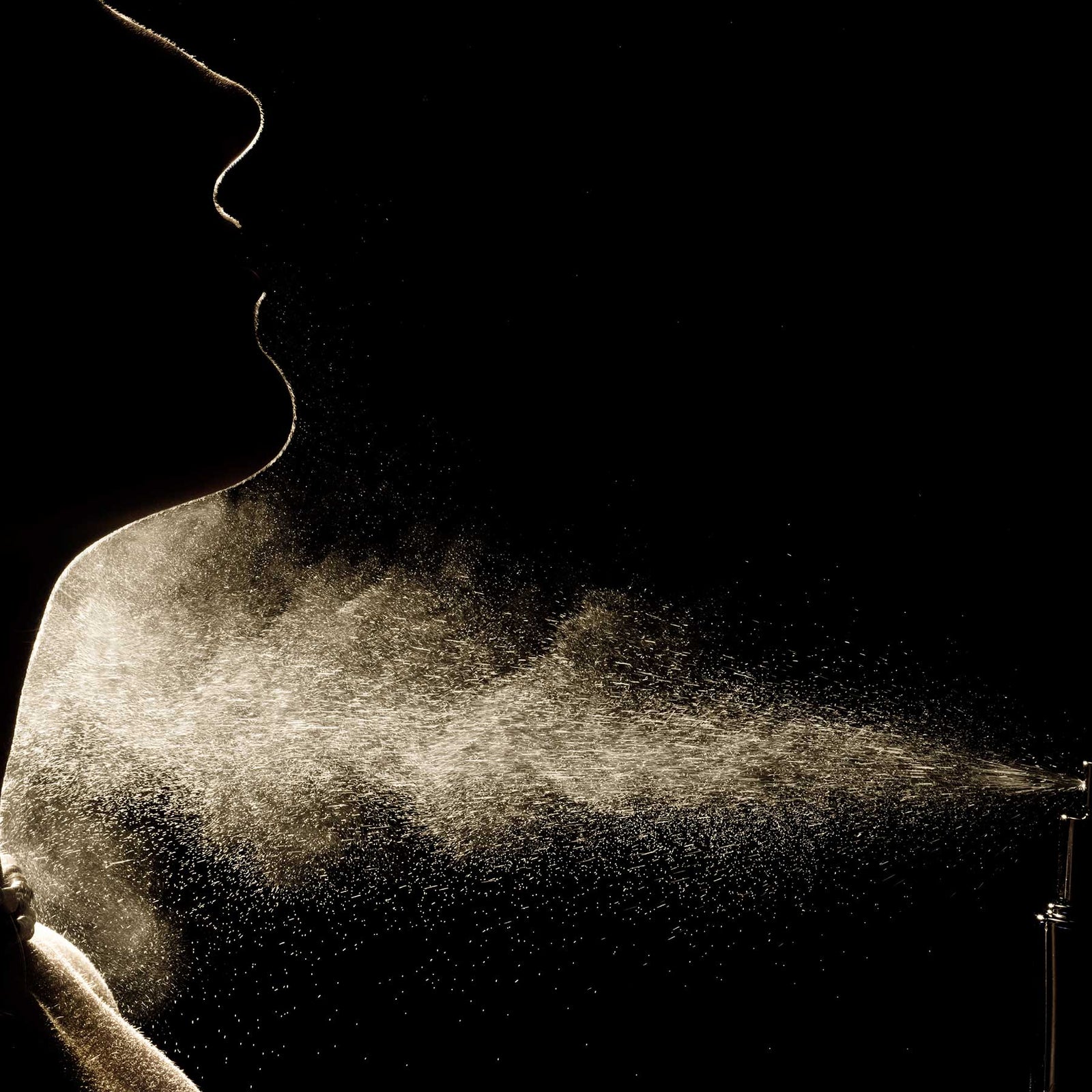 silhouette of woman spraying perfume on dark background