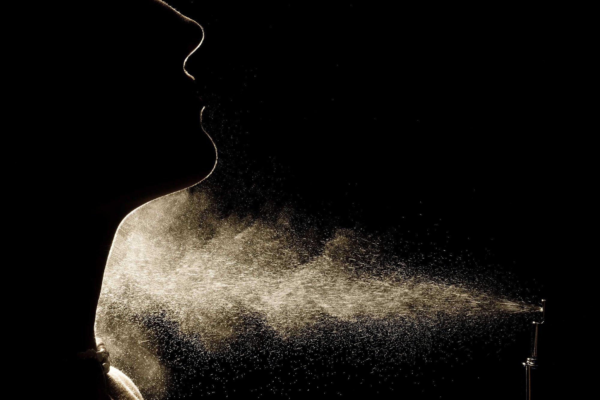 backlit silhouette of woman spraying fragrance on neck