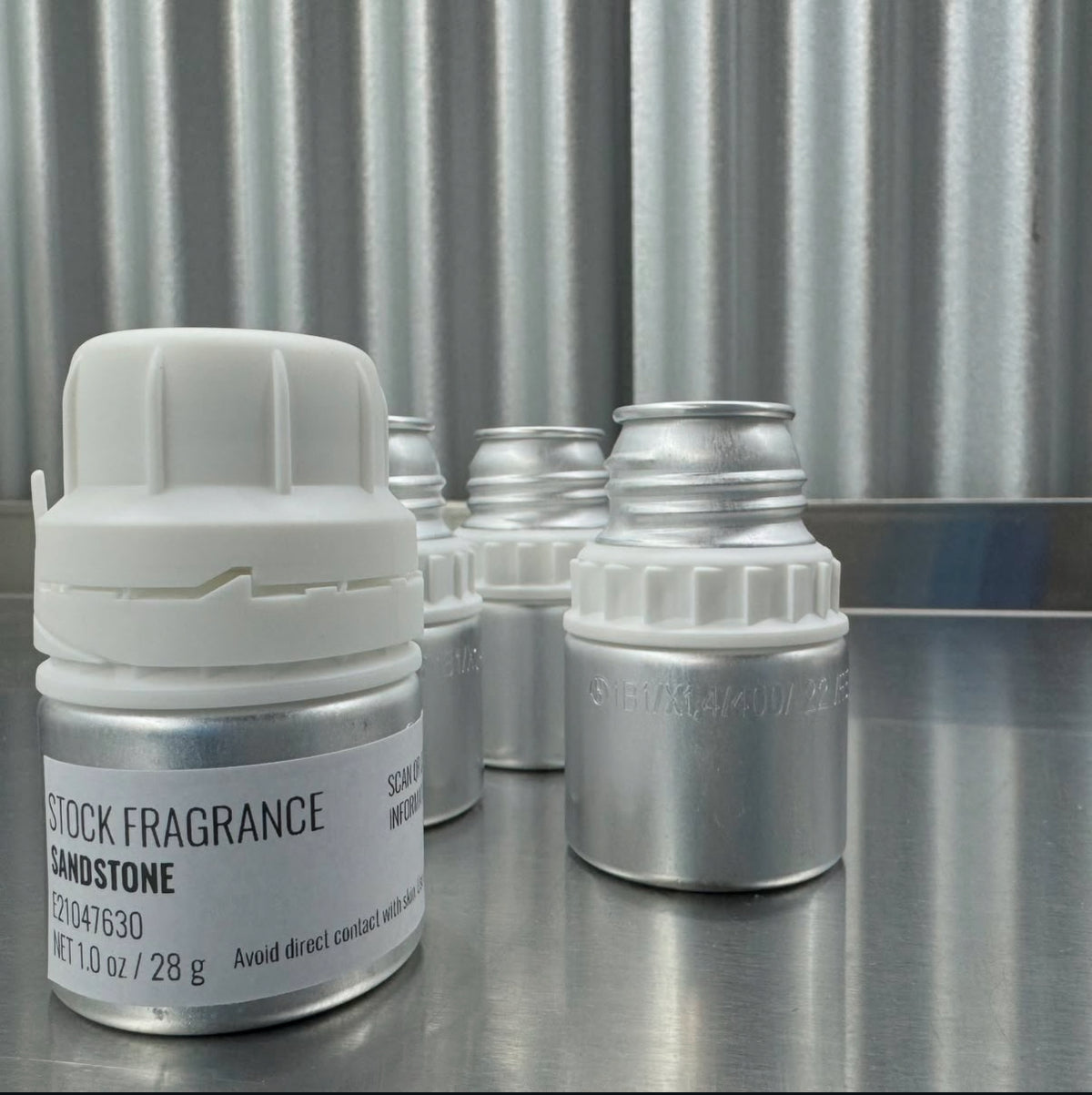 Set of small stock fragrance containers on a metallic surface with a corrugated metal background