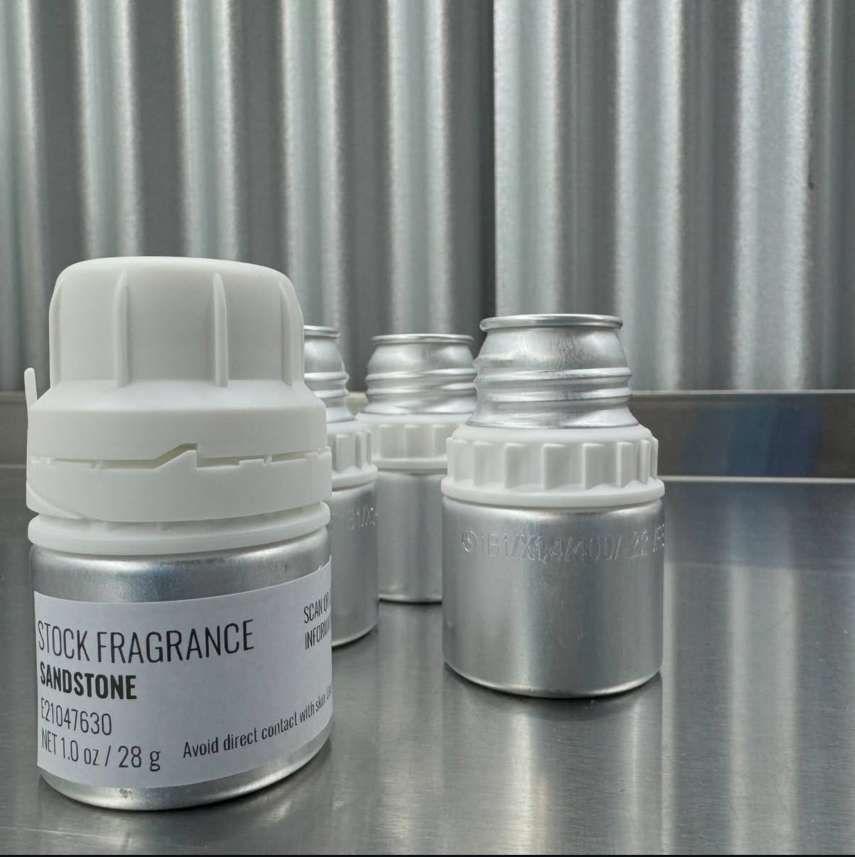 Set of small stock fragrance containers on a metallic surface with a corrugated metal background