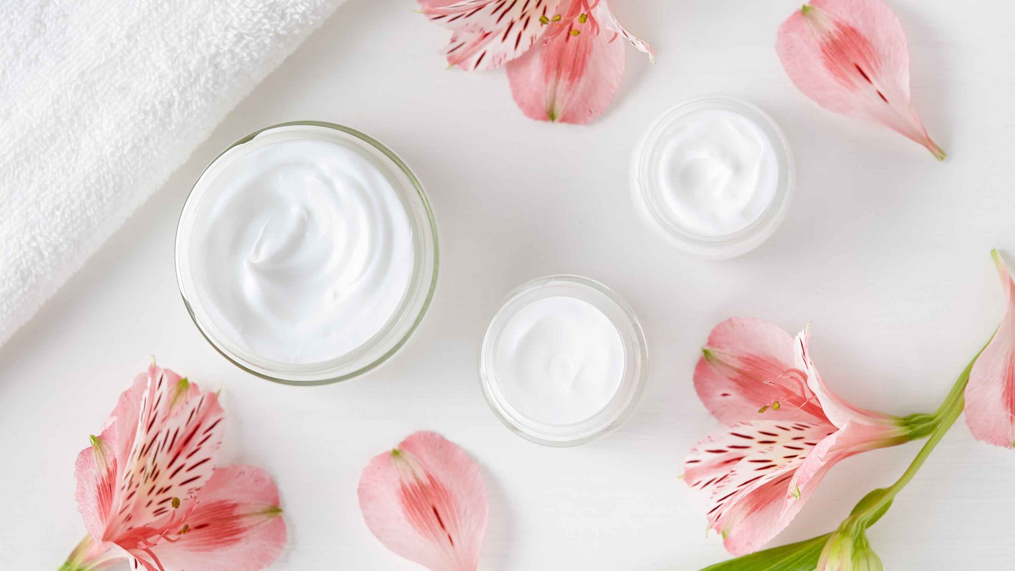 pink flowers and open beauty cream jars on white surface