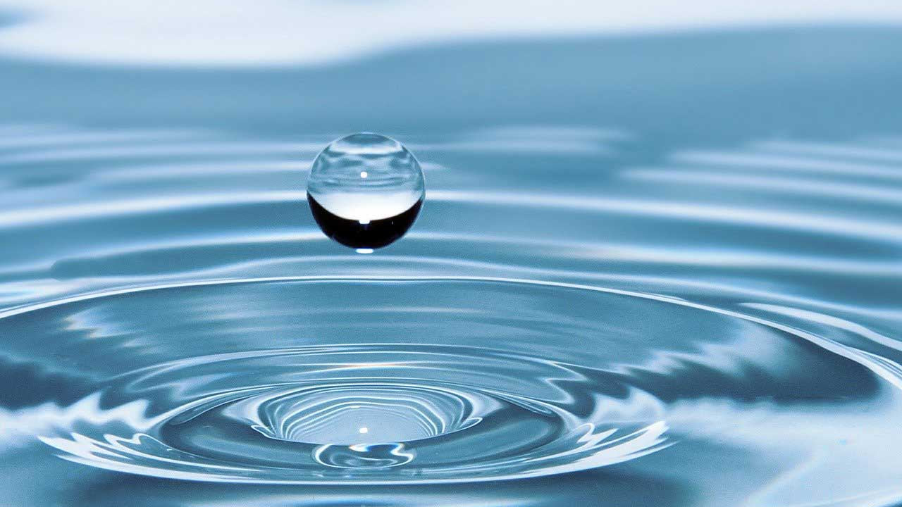 Water droplet falling into water with concentric circles.