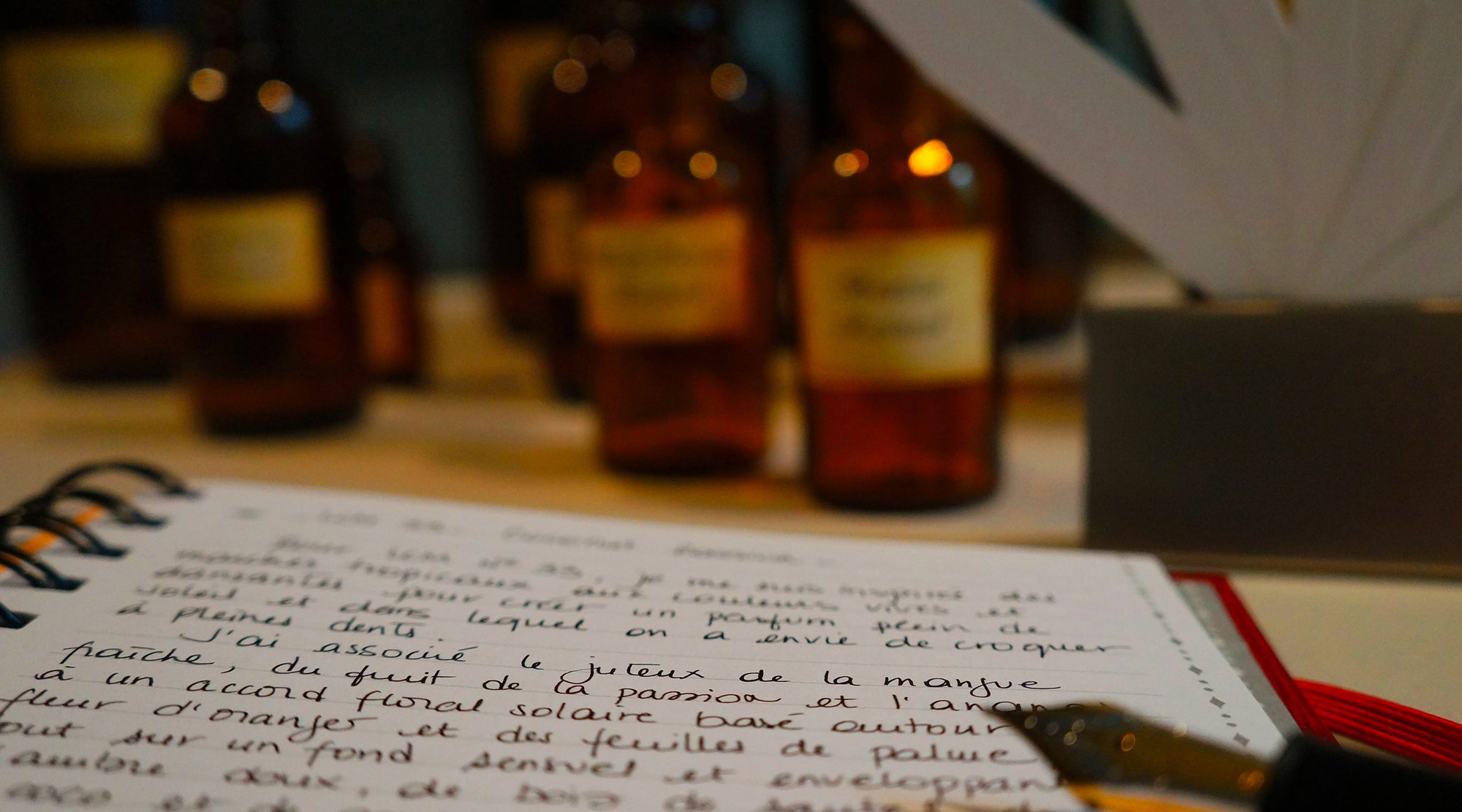 perfumer's notebook with handwritten notes in french and perfume bottles and blotters in background